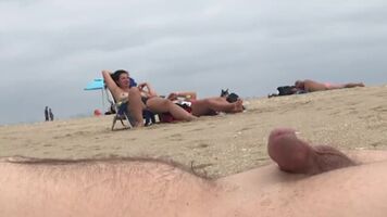 Guy pretends to be asleep on the beach while people watch him cum